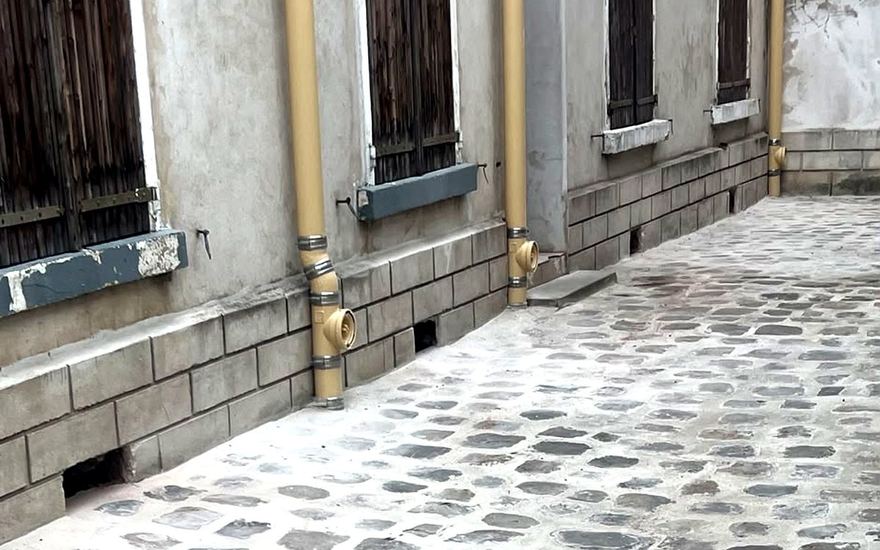 Descentes d’eaux pluviales et regards de visite installés dans une cour pavée d’immeuble