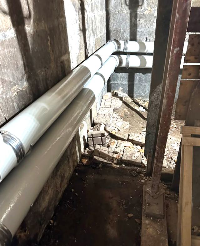 Collecteurs d’évacuation neufs posés le long des murs d’une cave d’immeuble